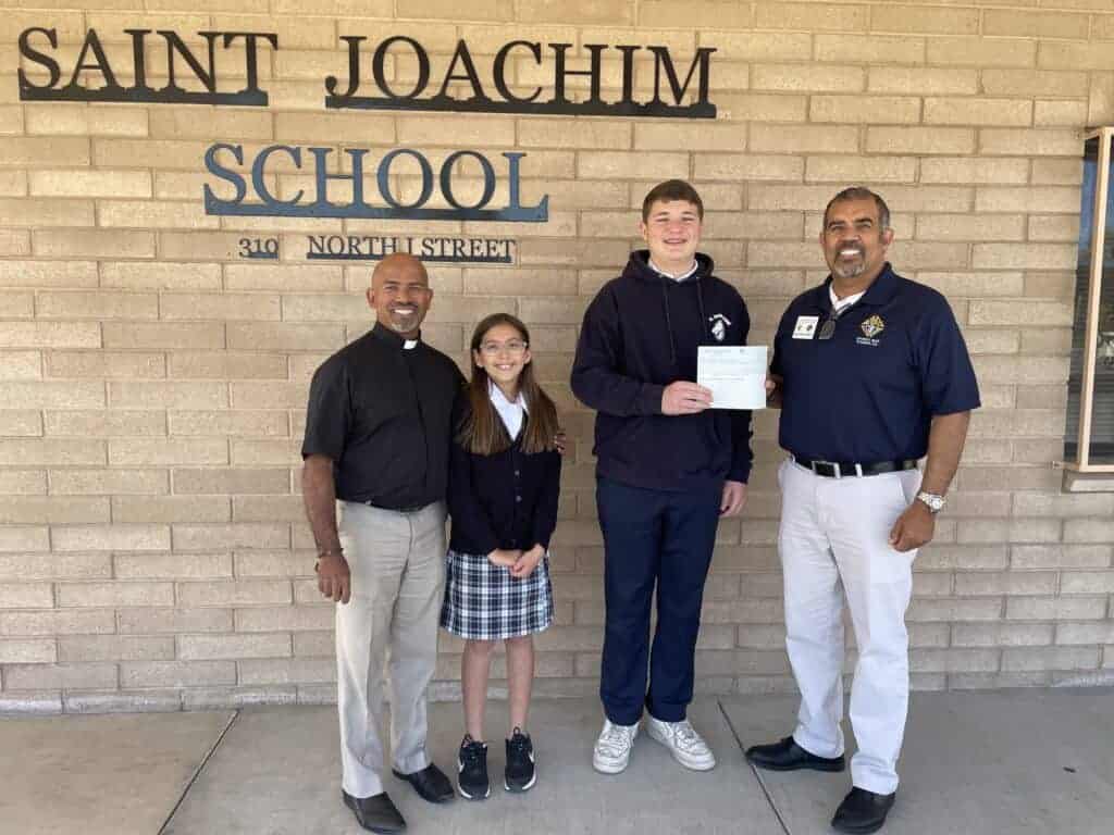 Photo - St. Joachim School student body president Eli Sablan presents the check to the Knights of Columbus Deputy Grand Knight Joseph Sanchez. With Sablan are Father Shaji and Arianna Castro.