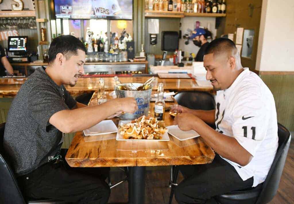 Photo - Brian Ponce, left, and Nabor Castillo enjoy an order of nachos and beer while indoor dining at Sugar Pine Smokehouse on Thursday. The restaurant is open from 8 a.m.-9 p.m. Monday-Thursday, 8 a.m.-10 p.m. Fridays, and from 7 a.m.-10 p.m. Saturdays and Sundays.