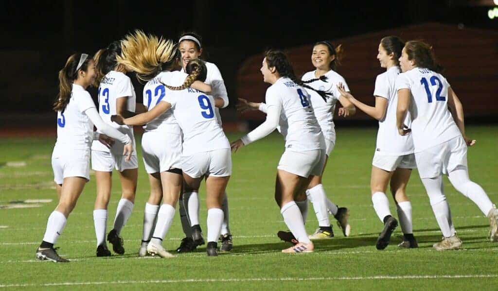Photo - The Madera Coyotes girls soccer team surround Jasmin Piñon (22) after she scored the eventual game-winning goal against the Madera South Stallions on Friday in Memorial Stadium.