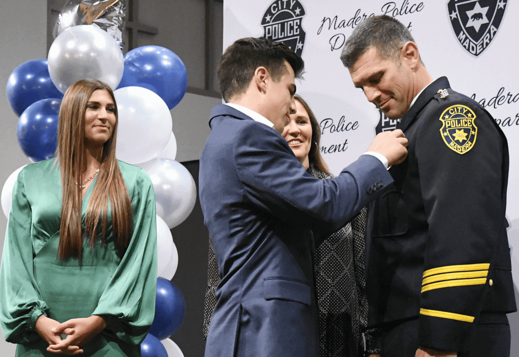 Photo - New Madera Chief of Police Gino Chiaramonte gets his badge pinned on by his son, Giovanni, while his wife, Shannon and daughter, Gianna, look on during a promotion ceremony Tuesday evening at Madera Avenue Bible Church.