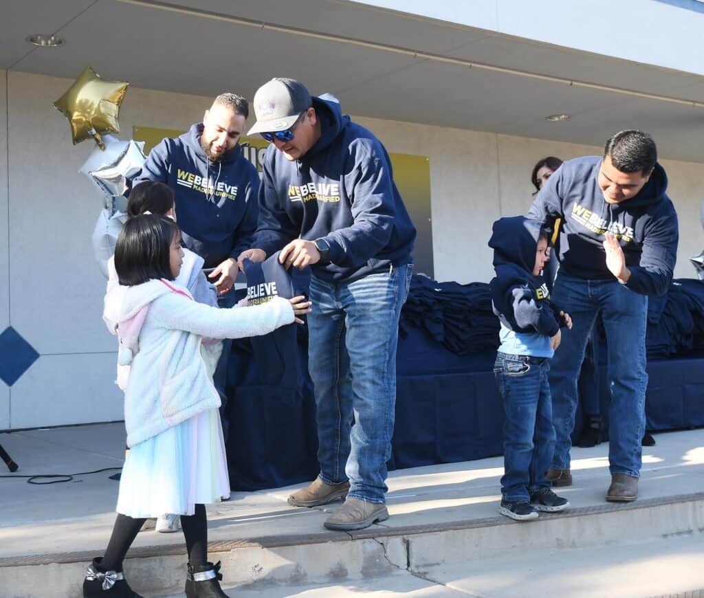 Photo - Mike Alamari, President of Pacific Farm Management and Cal-Pacific Supply Inc., left, Enrique Garcia center, and Martin Chavez hand out 100 hoodies of 500 to be distributed to students at Nishimoto Elementary School on Friday.