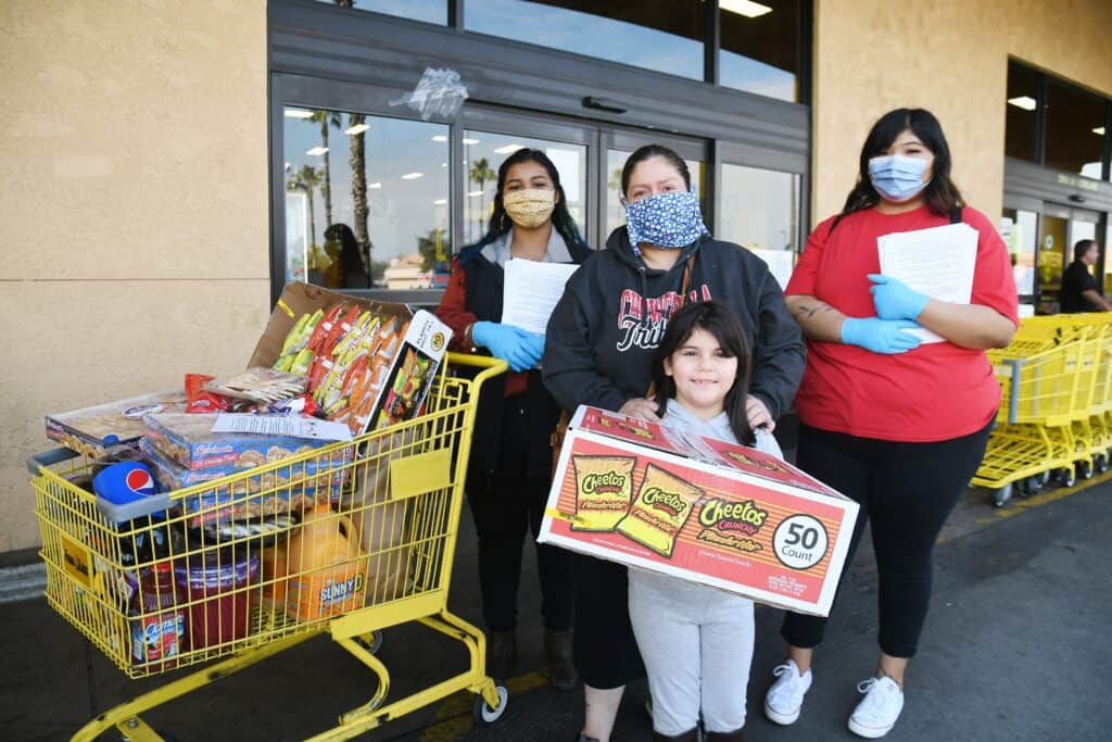 Photo - Jackeline Hernandez, left, and Le Shell Beas of AMB Ranch join Patricia and Bailey, 7, Venegas after a representative from AMB Ranch paid for their groceries on Saturday at Food 4 Less.
