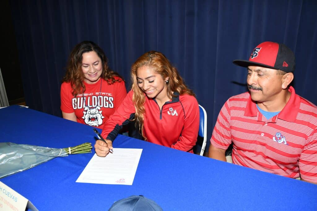 Photo - With her parents, Leticia, left, and Alfonso watching, Madera Coyotes softball standout Aaliyah Cuevas signs her National Letter of Intent to play softball at Fresno State in 2017. Cuevas’ junior season was canceled just before the Bulldogs started Moutain West Conference play.