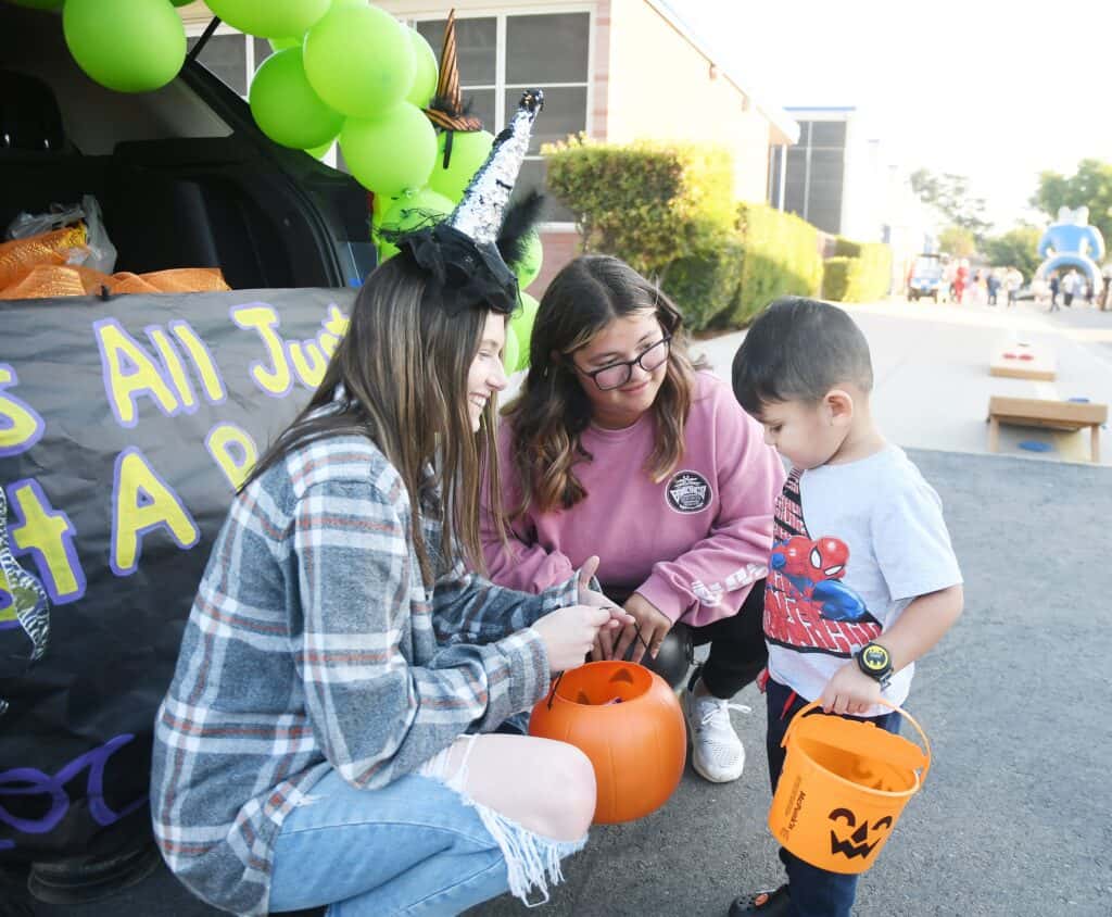 Photo - Kylie Bursey, left, and Sydney Fernandez of Madera High ASB give Liam Torres some candy during the Madera Unified School District’s Trunk or Treat hosted by Madera High School on Wednesday evening.