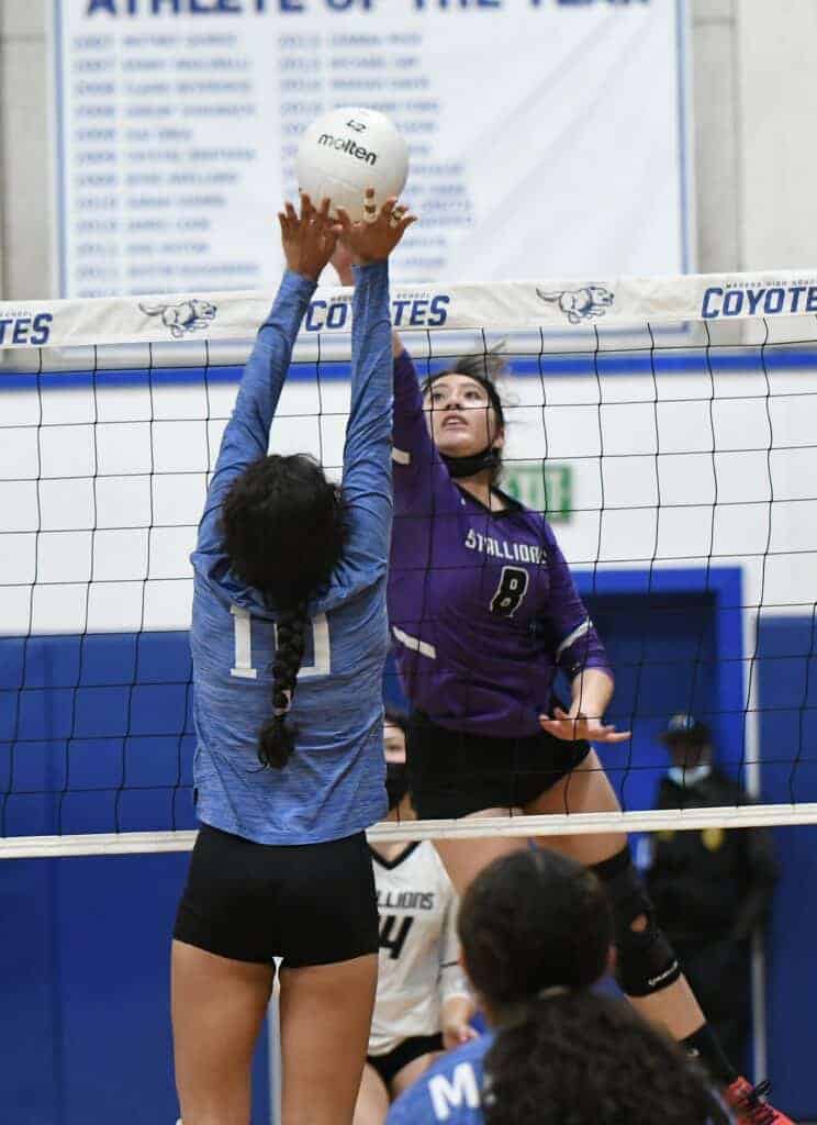 Photo - Madera South’s Jazlynn Vargas tips a ball past the outstretched hands of Madera’s Sabrina Mata during Tuesday’s rivalry match. The Stallions won in five sets while Vargas tied for the match high in kills with 16.