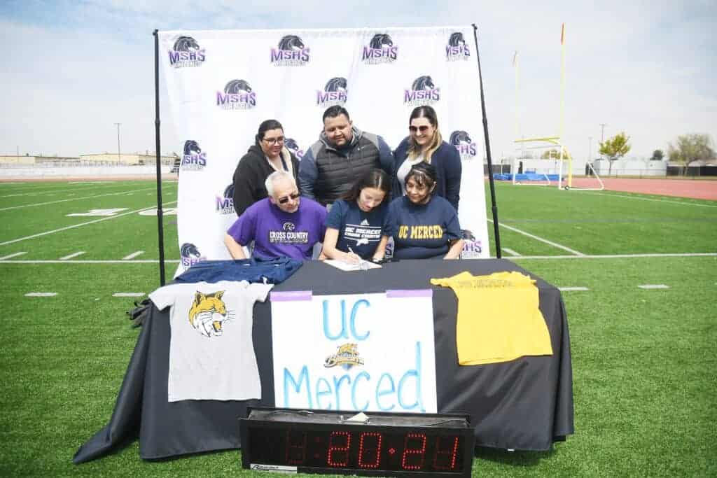 Photo - With her family surrounding her, Madera South cross country and track runner Jaydah Aguilar signs her National Letter of Intent to UC Merced in March.