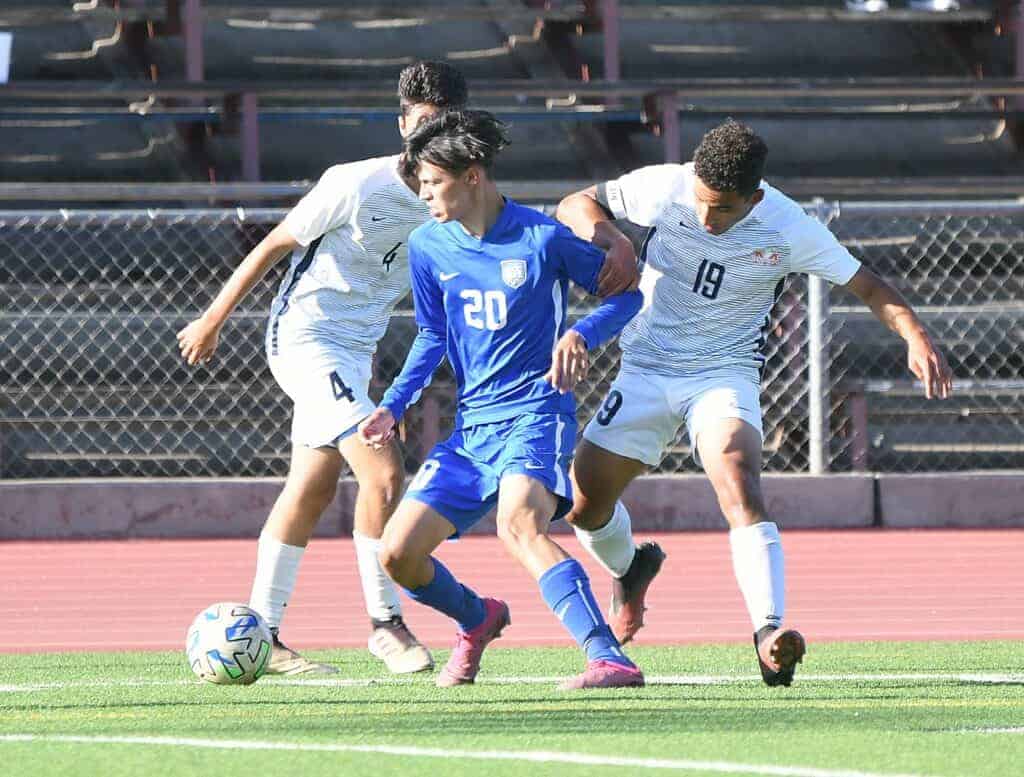 Photo - Madera senior William Bispham tries to dribble around a pair of San Joaquin Memorial defenders during Tuesday’s overtime loss.