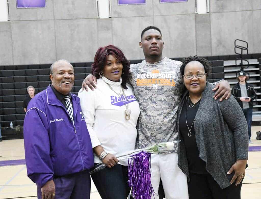 Photo - Kingsley Thomas stands with, from left, his grandfather James Murphy, mother Tarica Howard and grandmother Hazel during his 2018 boys basketball Senior Night. In September, Thomas and Howard saved Murphy’s life.