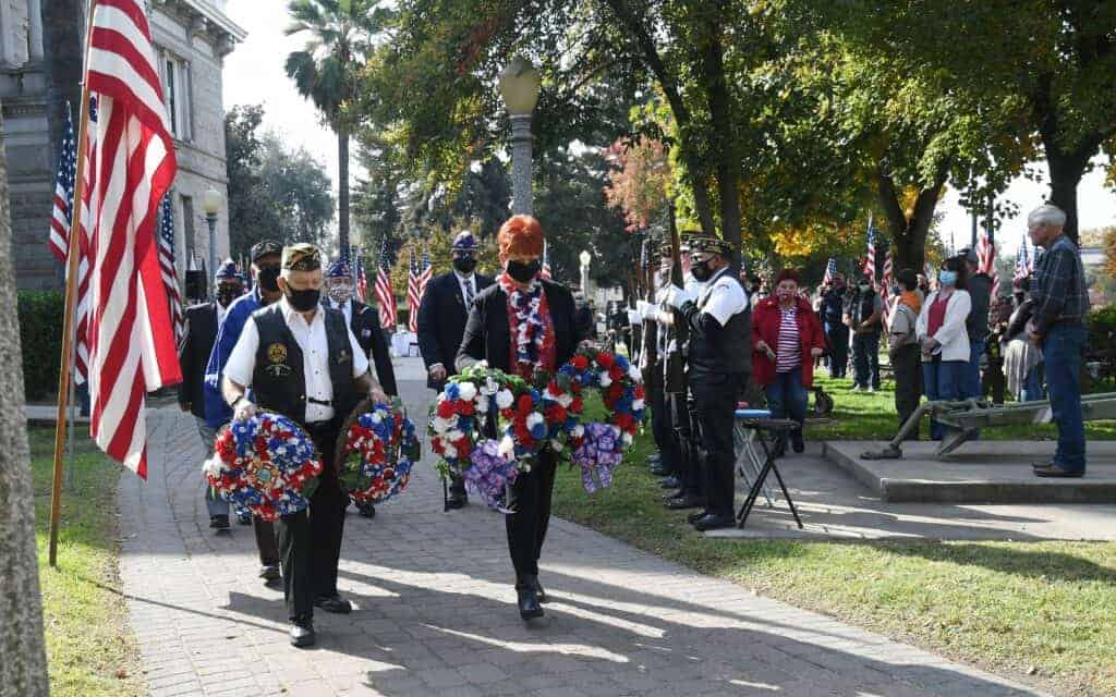 Photo - VFW Post 1981 Senior Vice Commander George Bloch and Auxiliary President Cindi Wood carry wreaths to be placed on the veterans memorial monuments during the Veterans Day Service at Courthouse Park.