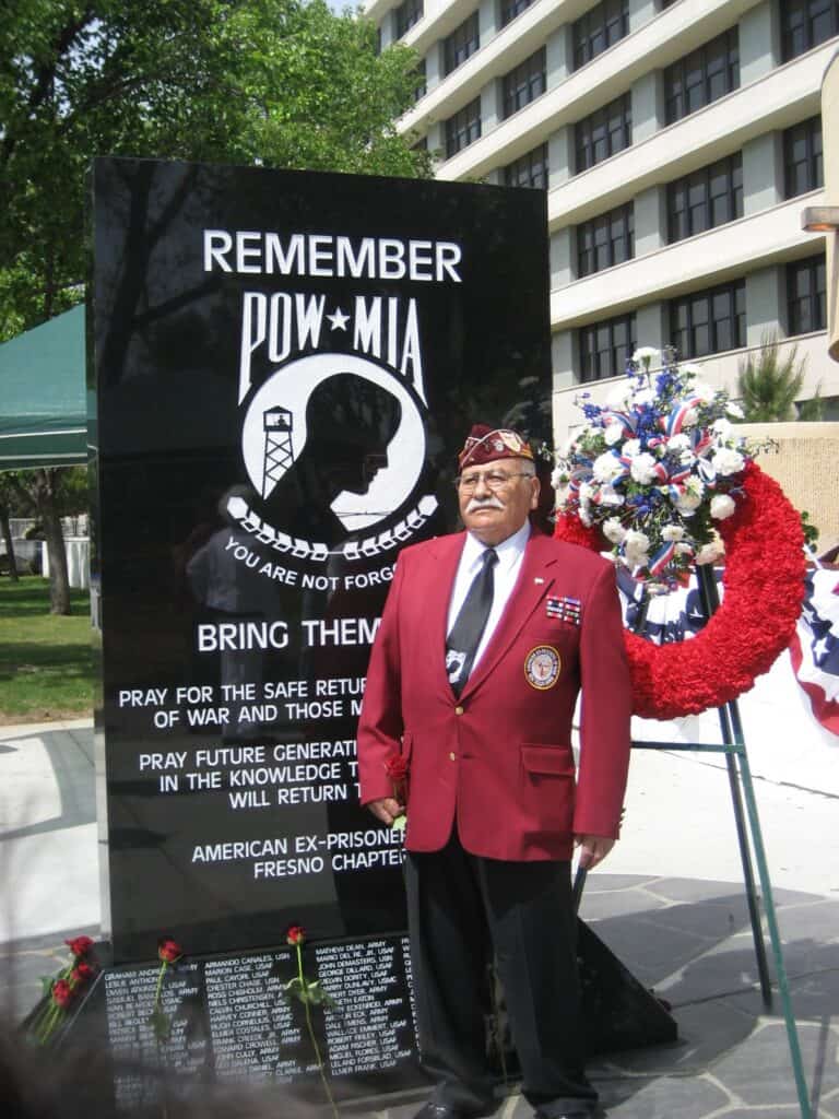 Photo - World War II Veteran Pasqual Reyes stands beside a monument honoring prisoners