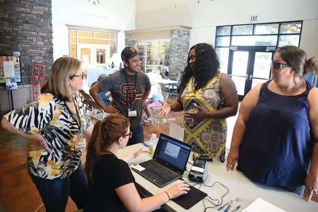 Photo - Voter Center representatives Kathie Rossi, left, Katarina Vandenack, seated, and Sal Hernandez assist voters Keysha Isler and Sarah Machado, right, at the John W. Wells Youth Center on election day.