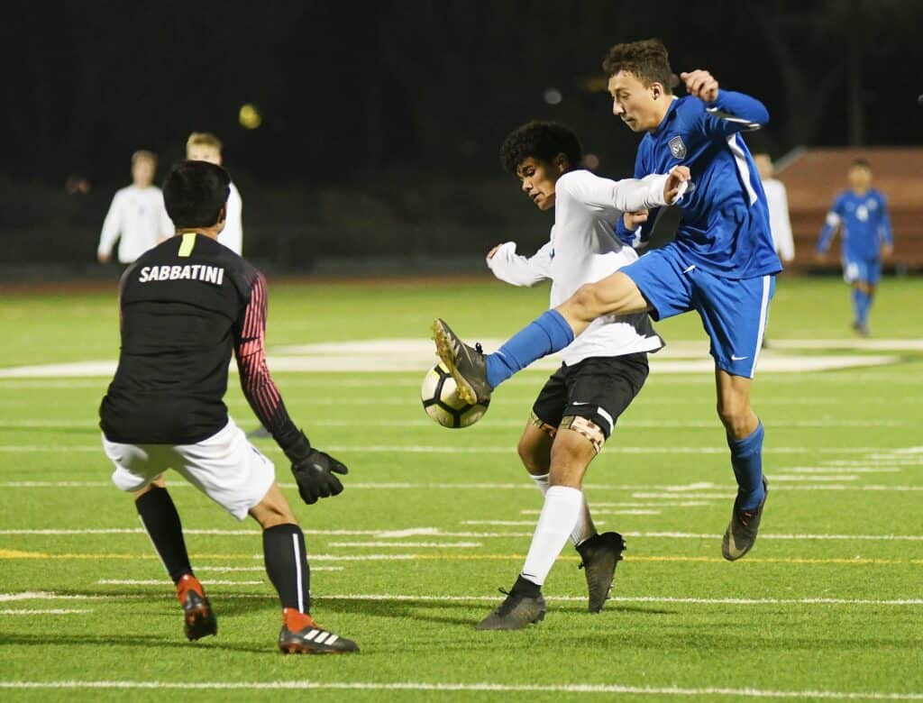 Photo - Madera’s Emmanuel Cabello, right, battles with a Clovis defender and the goalkeeper for a shot on goal during a 1-0 win over Clovis. Cabello scored the game’s lone goal to extend Madera’s winning streak to three.