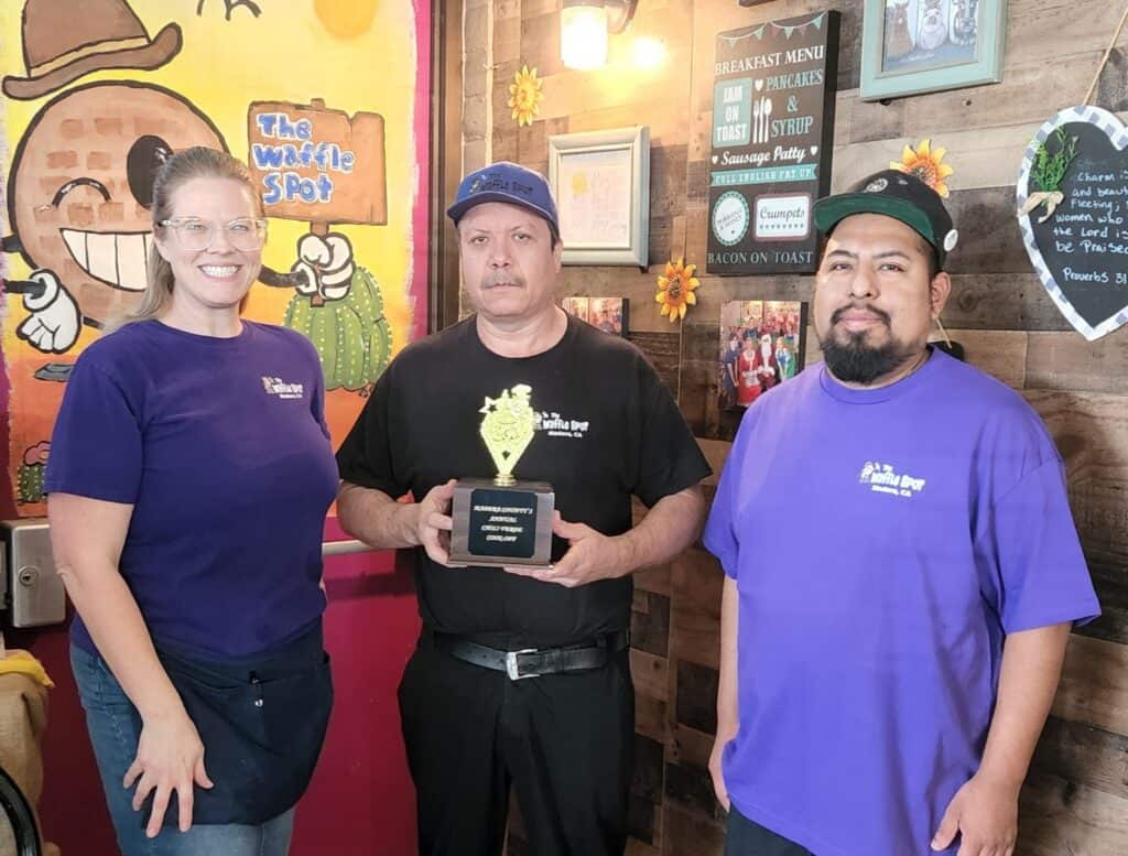 Photo - Waffle Spot owner Kim Praytor stands with her cooks Lolo Rivera, middle, and Juan Ruiz while they hold the trophy for next week’s Chile Verde Cook-Off.