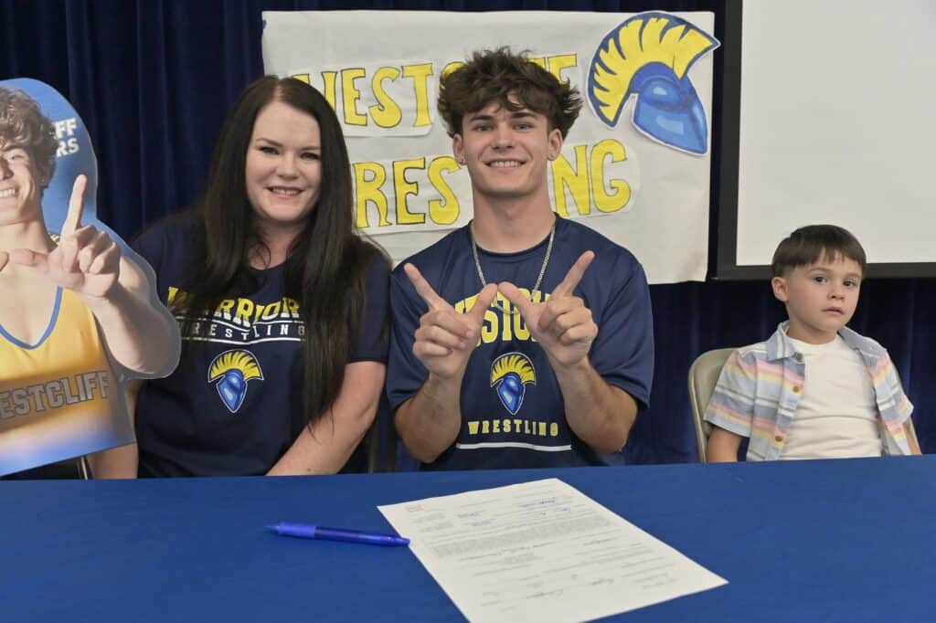 Photo - Madera wrestler Cameron Silber forms a ‘W” to indicate his school of choice, Westcliff University, after signing a National Letter of Intent. He is the first Madera wrestler to sign an NLI since James Cook in 2010.