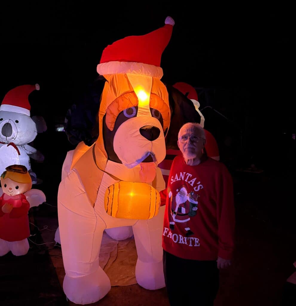 Photo - Coarsegold’s John Baker has been showcasing Christmas magic with his two-corner home display for many years. He stands with one of his favorite piece, a nine-foot tall St. Bernard inflatable. This is the final year of his magical display at 32370 Chickasaw Road.