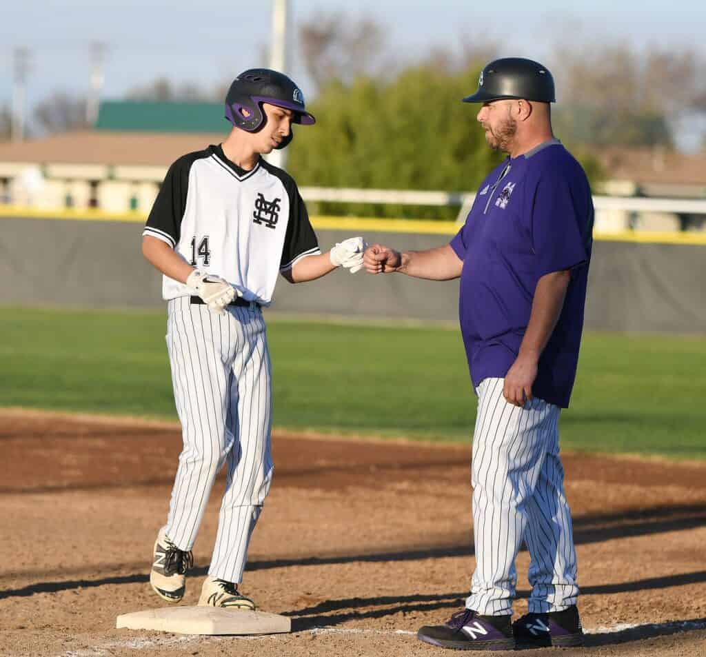 Photo - Madera South’s Anthony Gamiz gets a fist bump from first base coach Bo Bertoncini after his pinch hit single in the fifth inning during Wednesday’s 9-1 loss to the Dinuba Emperors at Eddie Chapa Field.