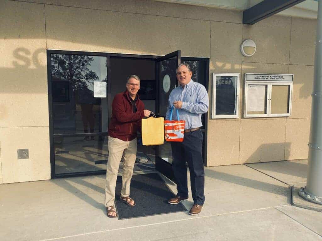 Photo - Madera Linkage Foundation president Tim Riché hands Sierra Unified School District superintendent Alan Harris a bag full of gift cards and other goodies donated by Madera Unified School District employees and students.