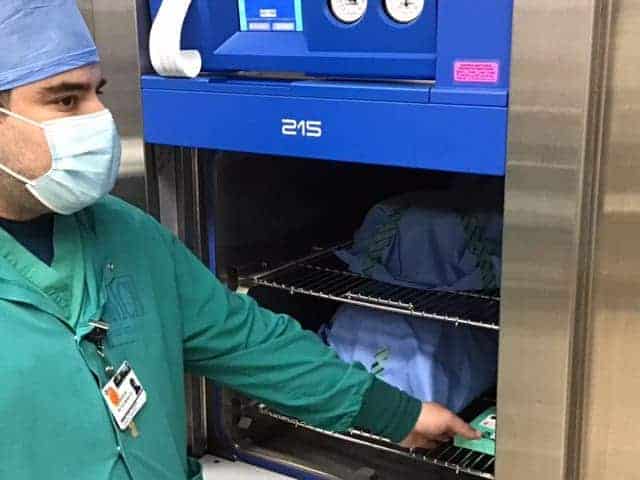 Photo - Reyes Mendoza, Central Supply Technician, at Madera community Hospital, removes a recently processed load of surgical devices. The tape documents the cleaning time and temperature range throughout the cycle.