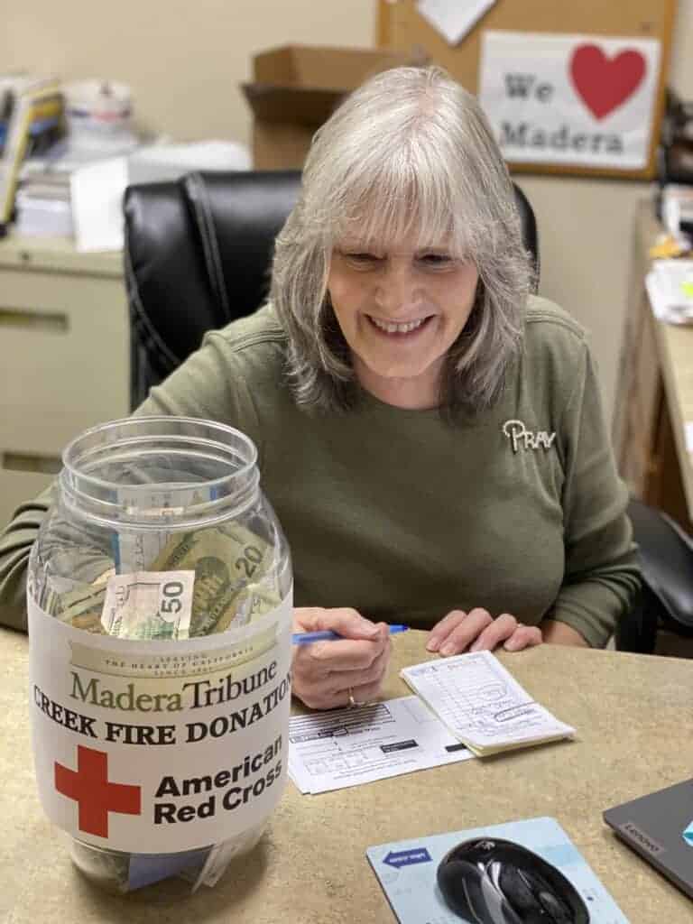 Photo - The Madera Tribune’s treasurer, Nancy Simpson, shown with the donation jar for the American Red Cross Creek Fire charity.