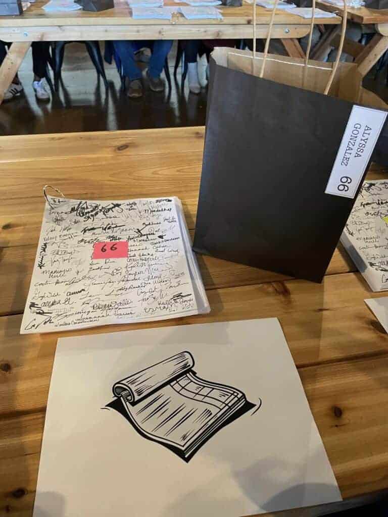 Photo - A copy of the “100 Pages” script in addition to a goody bag and an image of a hint as to what Alyssa Gonzalez’s page is about. Gonzalez contributed one page out of 100 writers for this project.