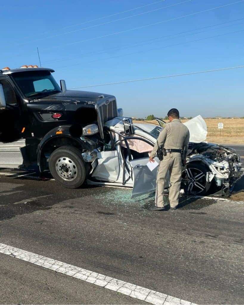 Photo - A Madera California Highway Patrol officer surveys the scene of a brig rig running into the back of a Honda Accord that set off a chain reaction crash Tuesday morning.