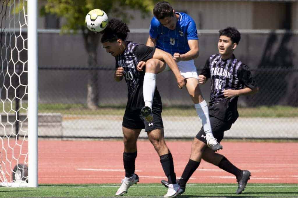 Photo - Madera South’s Aaron Ocegueda (20) heads a ball out of danger in front of a jumping Clovis player during Saturday’s loss with Marco Leal (17) providing support.