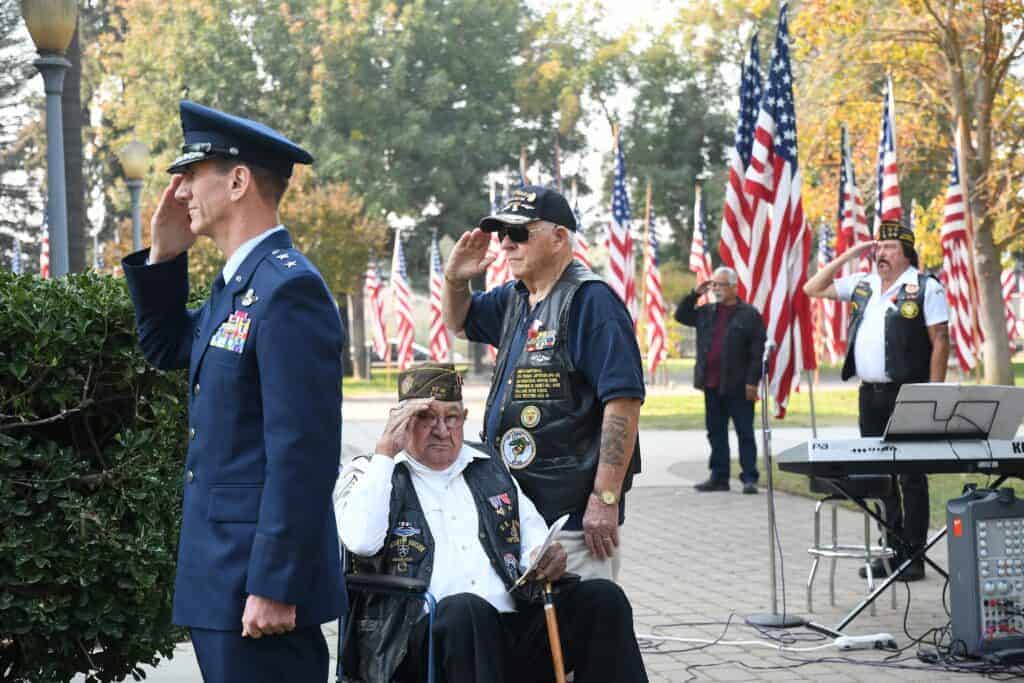 Photo - Honored guest speaker Major General Clay Garrison, Commander, California Air National Guard, left, and veterans Martin Medellin, seated, A. Michael De Cesare and Mokey Cowger salute during the annual Veterans Day Service at Courthouse Park on Sunday.