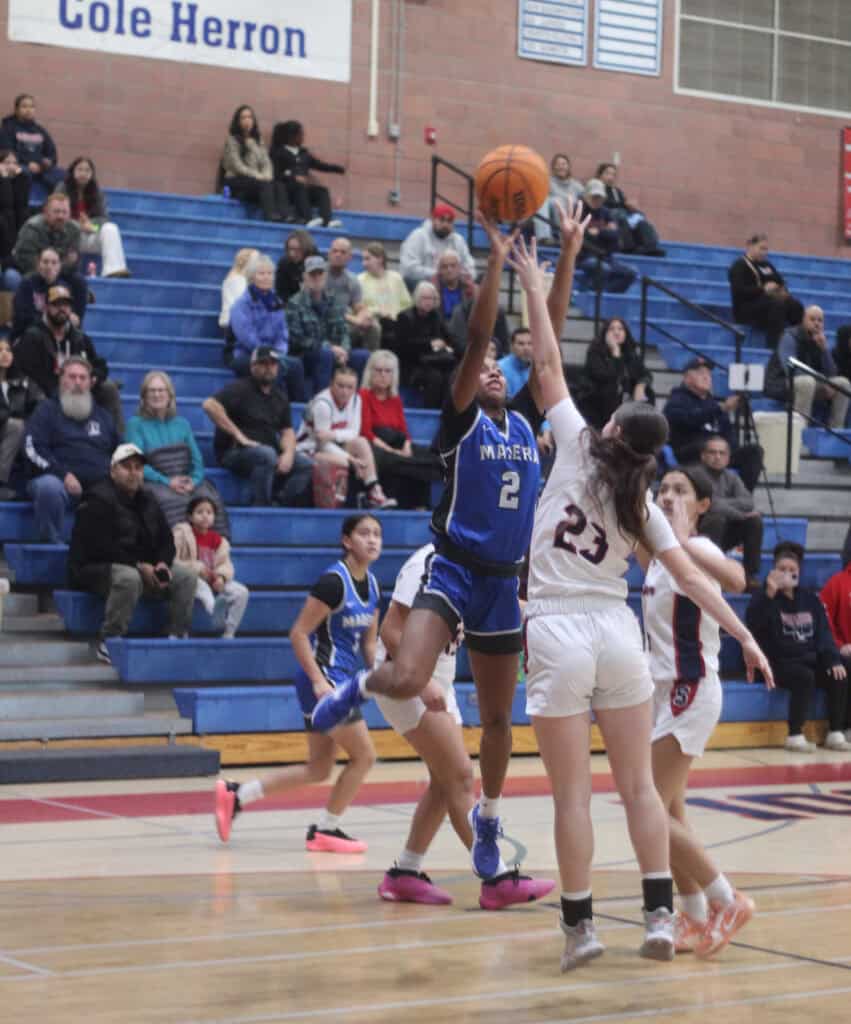 Photo of Madera freshman Janyah Spotwood shoots over a Sanger defender during the first half of Thursday’s road loss to the Apaches. Spotwood led the Coyotes with 15 points and 10 rebounds. 