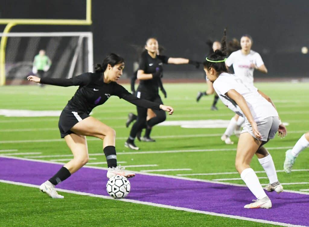 Girls soccer game on a green field with players in action.
