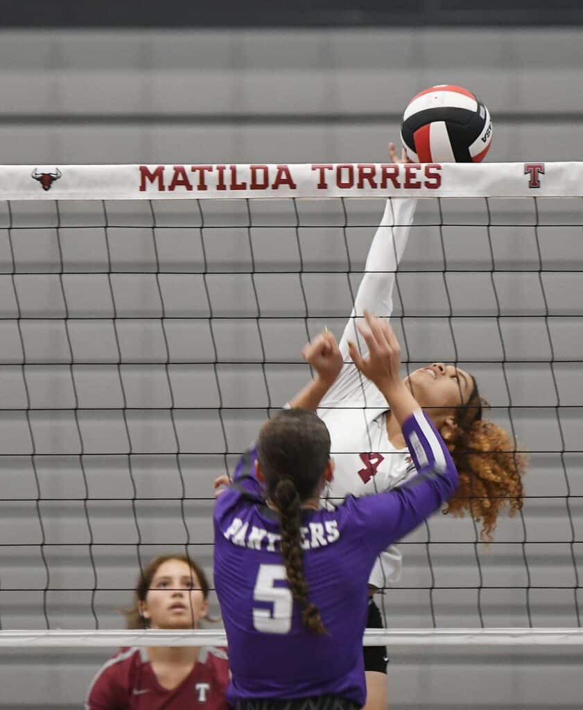 Young female volleyball player spiking ball at the net during game.