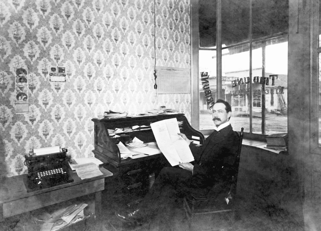 Man working at a vintage desk in a newspaper office, 1950s.