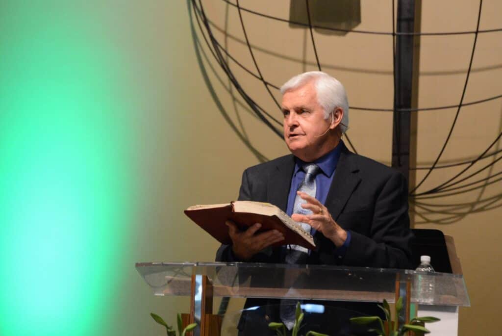 Man speaking at podium during Madera Tribune event, holding a book.