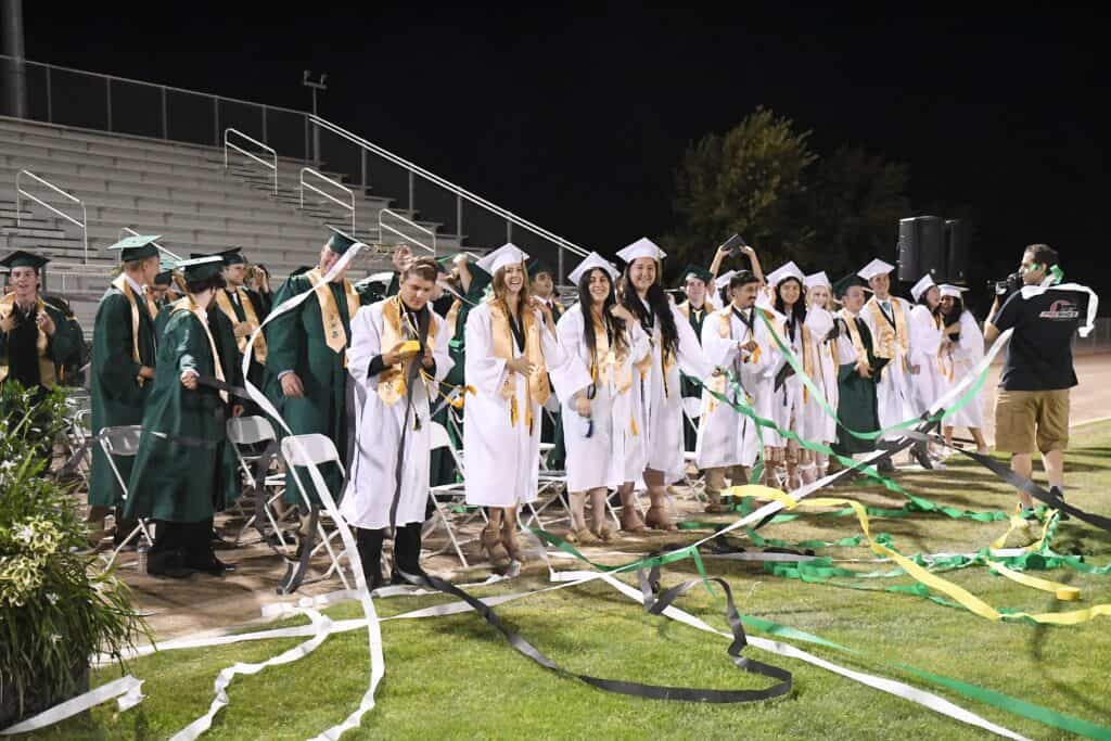 Graduates in caps and gowns celebrating graduation at Madera High School outdoor ceremony.