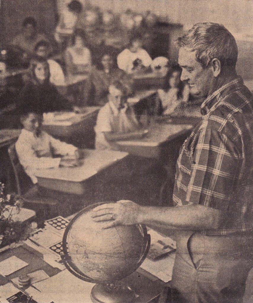 Teacher with globe in classroom full of students, educational setting.