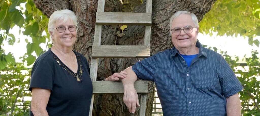 Elderly man and woman smiling outdoors near a tree, community leaders in Madera.