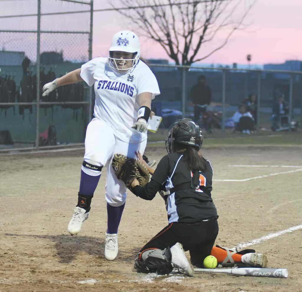 Female softball player sliding into home plate during game at dusk.