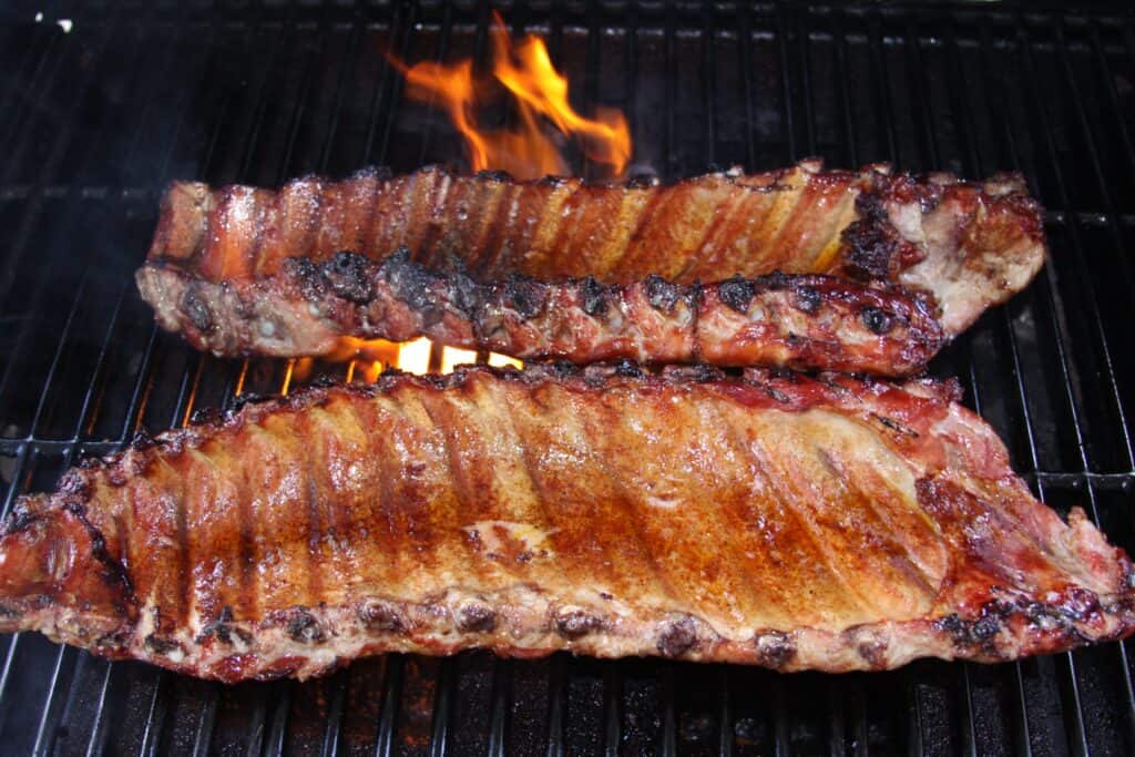 Grilled ribs on a barbecue grill with flames, showcasing delicious, smoky meat preparation.