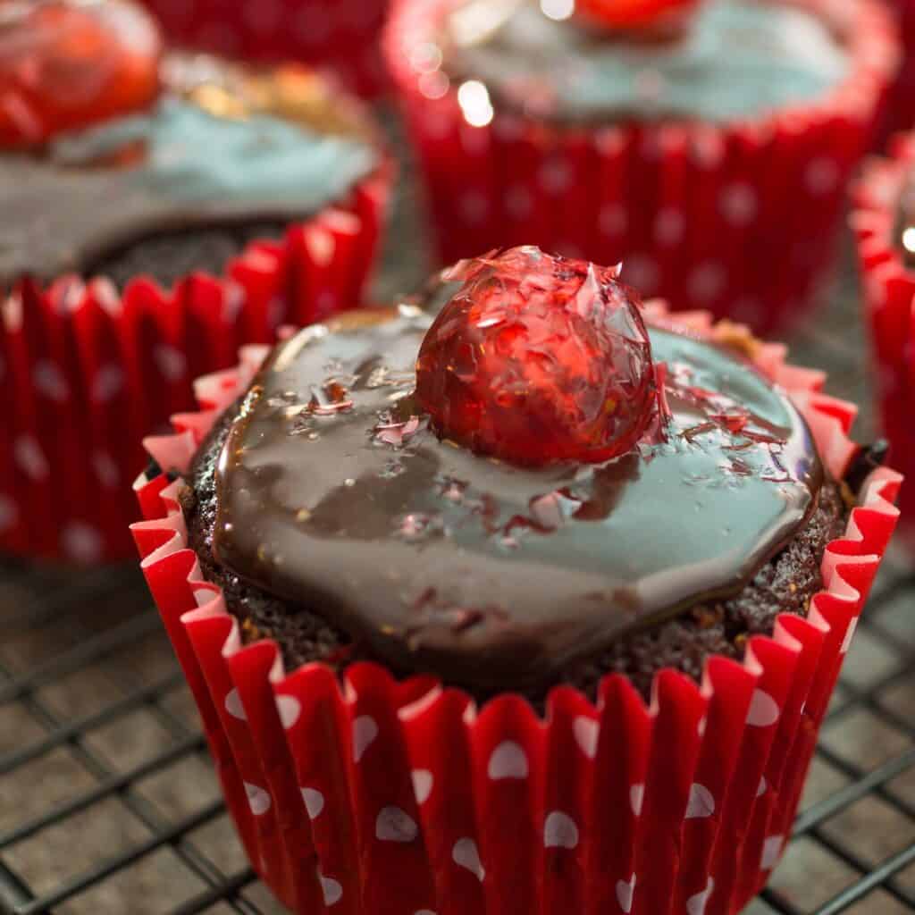 Chocolate cupcake with cherry topping and colorful frosting in red polka dot wrapper.