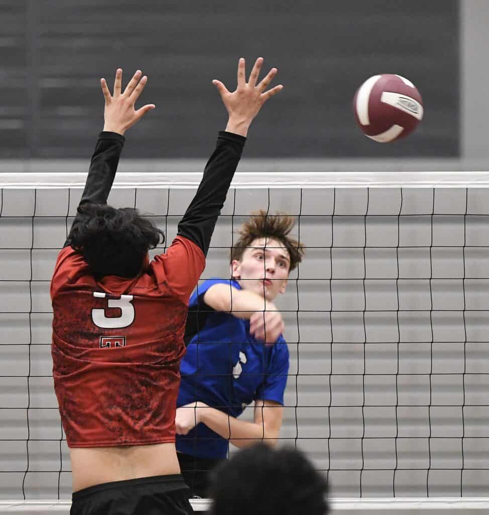 Volleyball players competing at the net during a match.