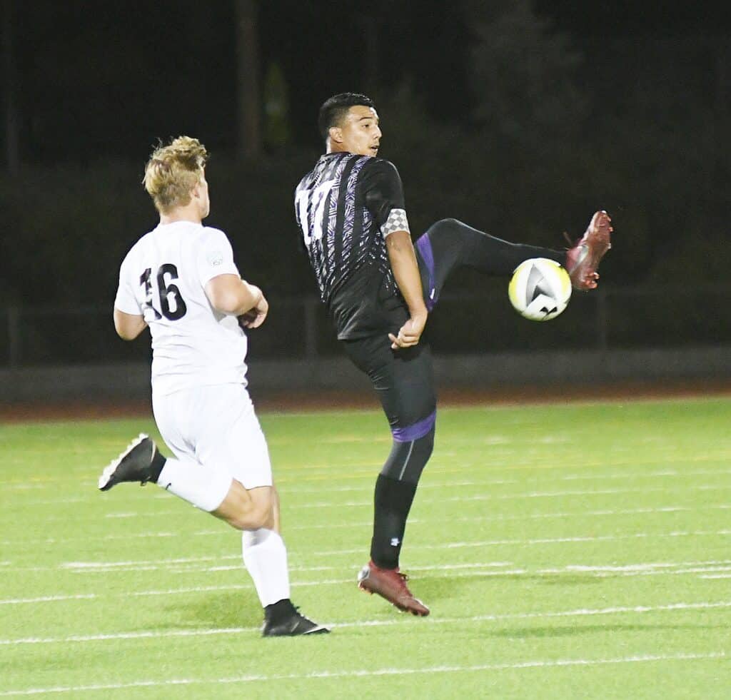 Soccer player kicking ball during night game on field.