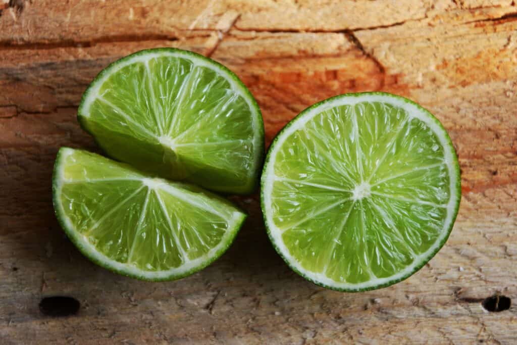 Lime halves on rustic wood surface, fresh and vibrant, ideal for cooking or garnishing.