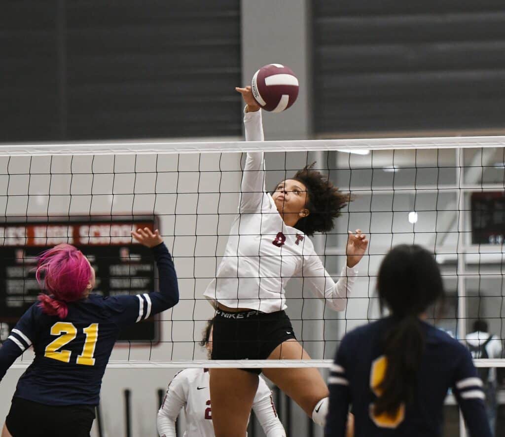 Volleyball player jumping to spike the ball at the net during a match.