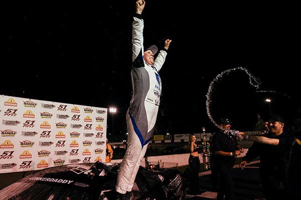 Race car driver celebrating victory on the podium at night.