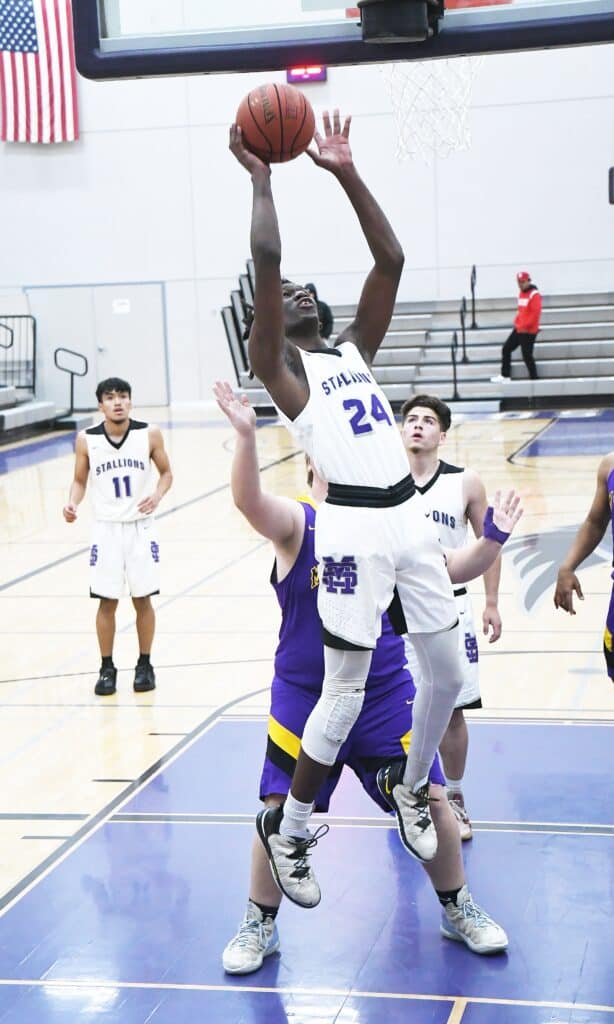 Young basketball player in white jersey jumping for shot during game.