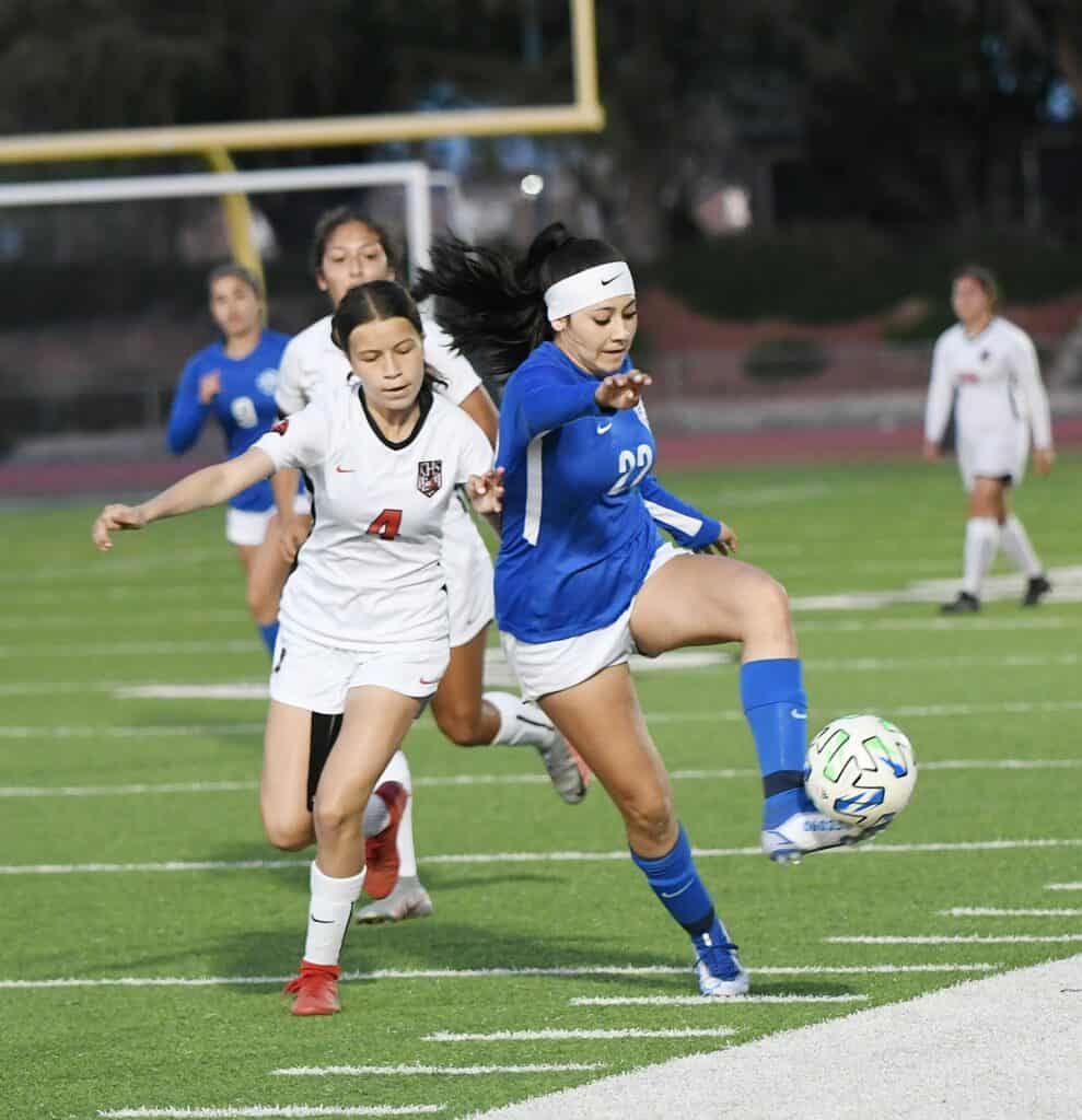 Girls soccer match with players chasing the ball on the field.