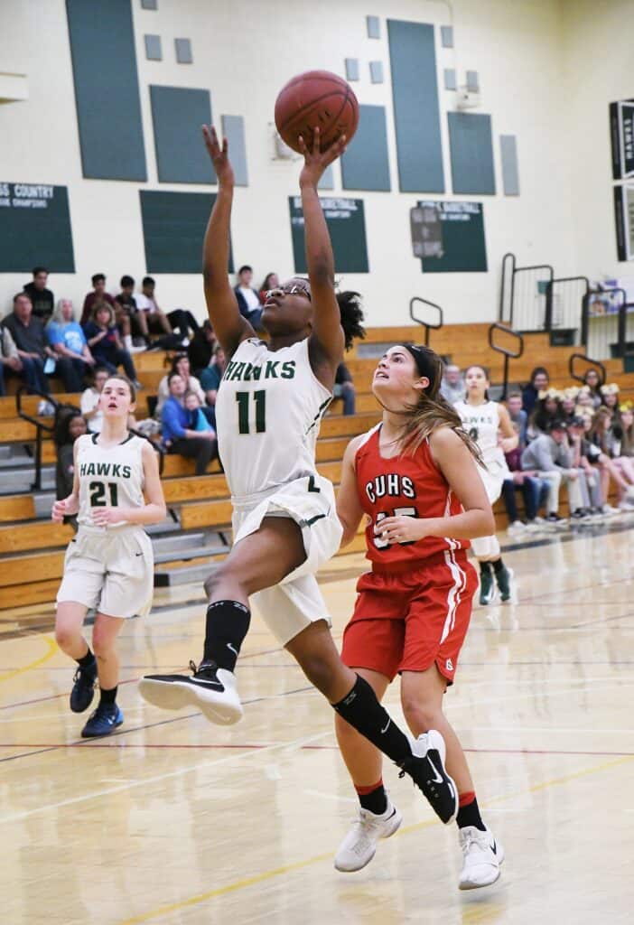Young female basketball player shooting during game in gymnasium.