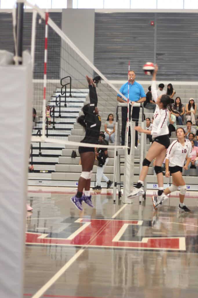 High school volleyball game with players jumping for the ball.