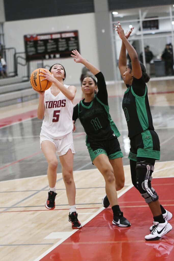 Young female basketball player shooting during game with defenders nearby.