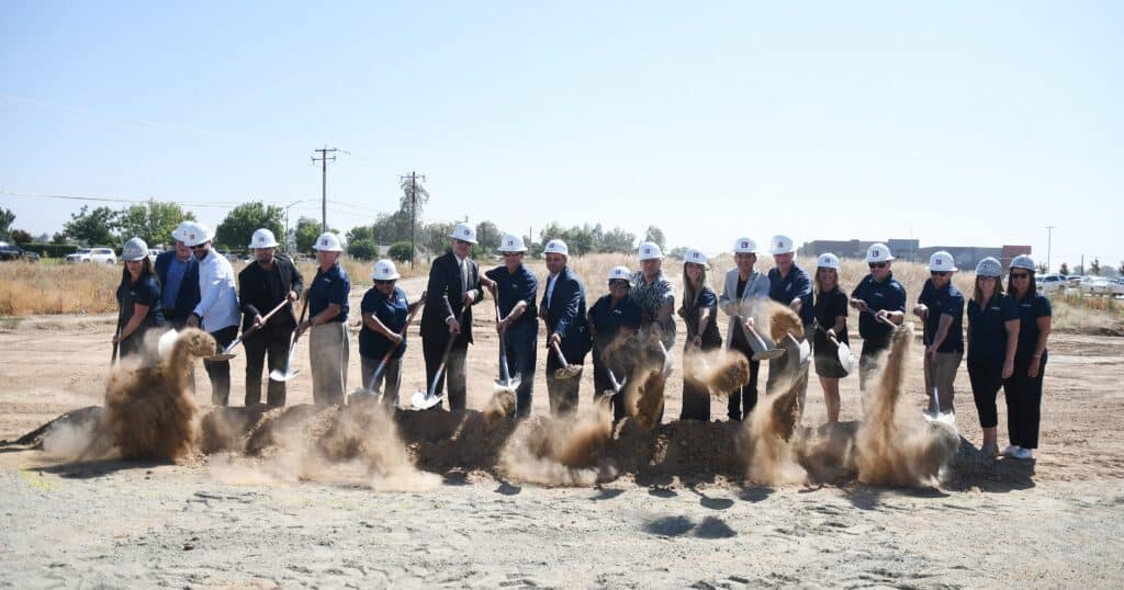Group of people at groundbreaking event with shovels and dirt.