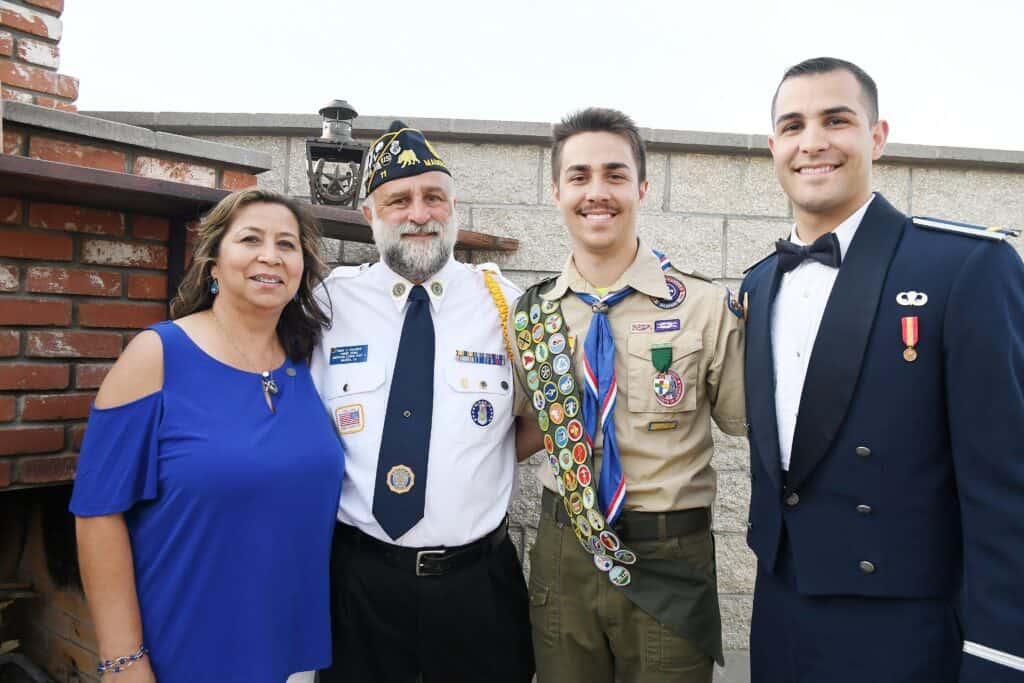Group of four people, including veterans in uniform, smiling outdoors.